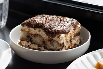 Close-up of tiramisu on a white plate under natural daylight, photographed in Shanghai, China