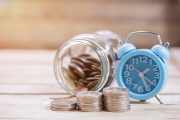 Close up saving money into a glass jar and alarm clock for cash in future investment.