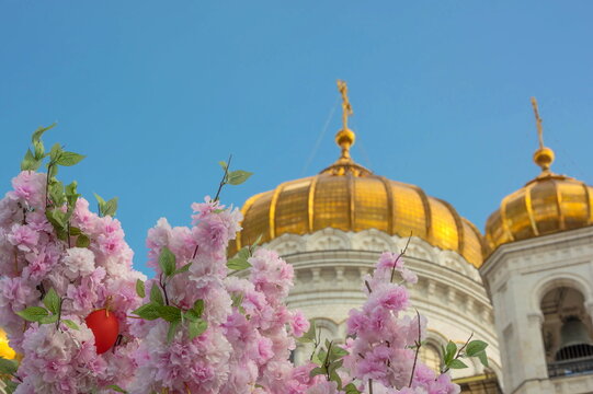 Delicate pink flowers and a red Easter egg on the background of the golden domes of the Cathedral of Christ the Savior