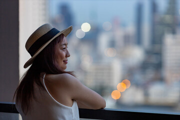 Asian woman tourist enjoying her urban city skyline from the hotel room balcony for vacation and...