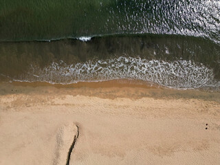 Overhead drone view of the serene interaction between gentle waves and the soft sandy beach,...