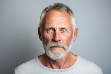 Obraz premium Portrait of a senior man with white beard and mustache looking surprised while standing against grey background