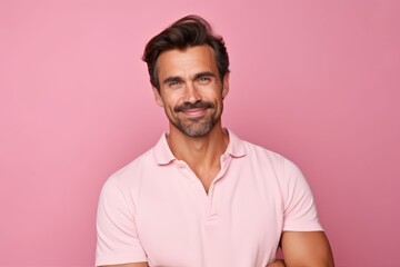 Portrait of handsome man in casual clothes looking at camera and smiling while standing against pink background