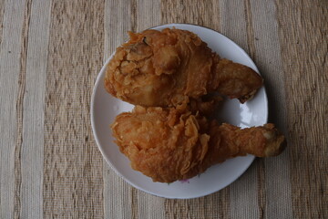 Two crispy fried chicken thighs on a white plate on a wooden table. Crypse flour fried chicken