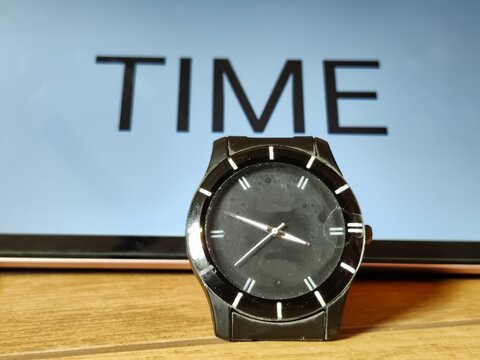 Picture of an elegant black wrist watch shot against time written on a placard in blur background