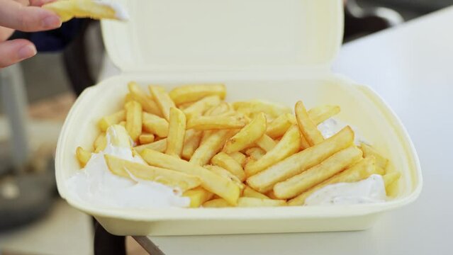 Picking up french fries and dipping them in mayonnaise on disposable disposable clamshell container, static closeup