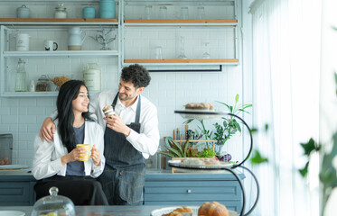 A husband wears an apron while cooking dinner with his wife. The duo took a break to sip coffee and sample the completed bread.