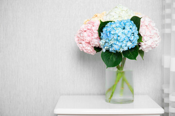 Beautiful hydrangea flowers in vase on white bedside table near light gray wall. Space for text