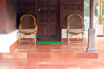 Heritage house entrance with peaceful and green surrounding. Cane chairs are placed outside the wooden house for relaxation. Place for old age home, relaxation, rehabilitation.