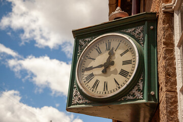 Fototapeta na wymiar An ornate vintage clock mounted on a brick wall, displaying time under a clear blue sky with wispy clouds