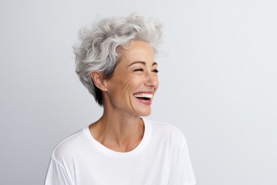 Cheerful senior woman with grey hair laughing over grey background.