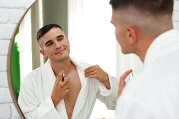 Obraz premium Handsome young man applying perfume in the bathroom