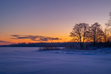 Fototapeta na wymiar A beautiful winter sunrise scenery of frozen lake and forest. Colorful landscape with dawn skies in Northern Europe.