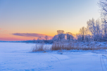 A beautiful winter sunrise scenery of frozen lake and forest. Colorful landscape with dawn skies in Northern Europe.