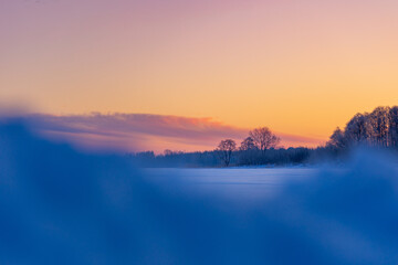 A beautiful winter sunrise scenery of frozen lake and forest. Colorful landscape with dawn skies in Northern Europe.
