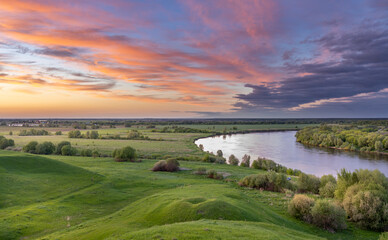 Fototapeta premium dramatic sky, colorful sunset, river bend against green field background, sunset landscape