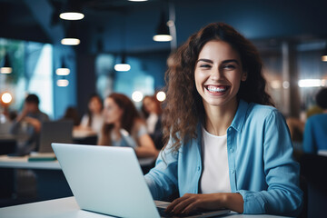Young cheerful woman sitting in front of computer in casual clothes, smiling and working late at night at office. Looking at camera.