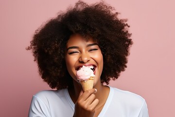 African young woman with a lush hairstyle eats ice cream in a waffle cone and smiles happily on a pink background - obrazy, fototapety, plakaty