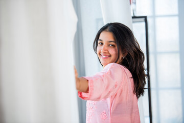 Indian pretty girl opening white window curtains view from side