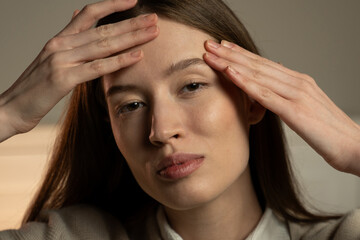 A close-up depicts a young woman with a serene expression, gently resting her fingertips on her temples. She gazes softly out of frame, against an understated background that suggests a moment of calm
