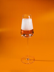 A glass of beer stands on a table with an orange background.