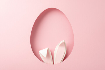 Imaginative Easter scene displayed from top view, with charming bunny ears visible through egg-inspired opening set against gentle pink background, providing space for heartfelt greetings or advert