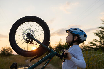 face of a boy in a bicycle helmet with a bicycle against the backdrop of the sunset sky and sun....