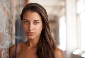 Zelfklevend Fotobehang Portrait, serious and woman by brick wall for confidence or casual fashion in corridor alone. Face, skin or young student, girl and hair of female person in hallway for profile picture in Argentina © peopleimages.com