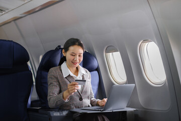 Asian female using laptop computer and holding credit card in airplane, Business traveling and...
