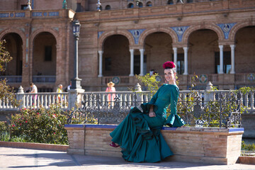 Fototapeta na wymiar Young, pretty, blonde woman in typical green colored flamenco suit, posing sitting on a tiled and brick bench. Flamenco concept, typical Spanish, Seville, Andalusia.
