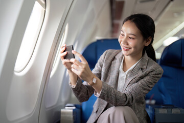 Asian young businesswoman successful or female entrepreneur in formal suit in a plane sit in a business class seat and uses a smartphone during flight. Traveling and Business concept