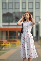 Portrait of a young beautiful red-haired girl in a dress in a summer park.