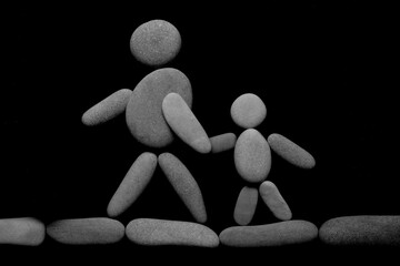 father or mother holding hand with small child made from many pebbles stones. silhouettes isolated on black background. Man or woman and Girl or boy Walking together