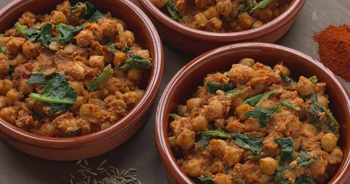Homemade Spinach and Chickpeas (Espinacas con Garbanzos) withingredients (cumin seed and smoked paprika spices, roasted almonds) on a table . Famous andalusian dish. Table spin.