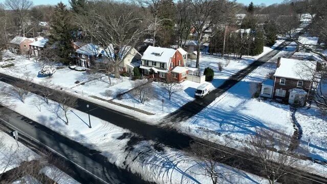 Snowy Suburb in american housing area in winter snow. Sunny day with snow covered roof of houses. Aerial approaching shot.