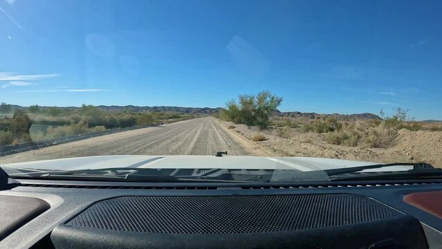 POV - Driving on gravel road in Mittry Lake Wildlife Area near Yuma AZ in Sonoran Desert in southwest Arizona on a bright, sunny day; dash and hood of the vehicle are visible