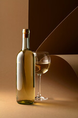 Bottle and glass of white wine on a beige background.