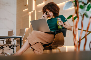 Woman using laptop drinking green smoothie with bamboo straw in the office