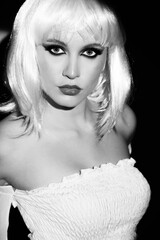 Fashion concept. Beautiful slim woman with gorgeous body and white wig wearing tight white clothes. Model with smokey eye shadows looking at camera with seductive look. Black and white image