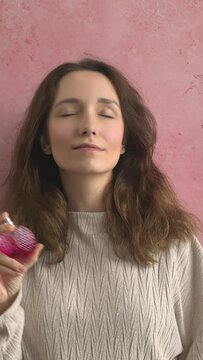 Girl using perfume in a pink bottle feeling confident and attractive. Pink background with copy space. Vertical video.