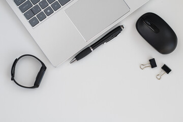 Close-up of a silver laptop with black pen, black smartwatch and black mouse on an office desk.