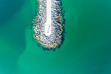 Aerial zenithal drone view of a breakwater in a sea of turquoise water