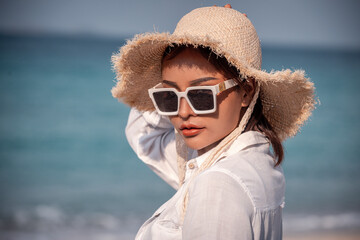 Portrait beautiful Asian woman wearing Bikini ,white t-shirt, sunglasses and straw hat at beach on vacation looking away while enjoying sea breeze is summer vacation concept.