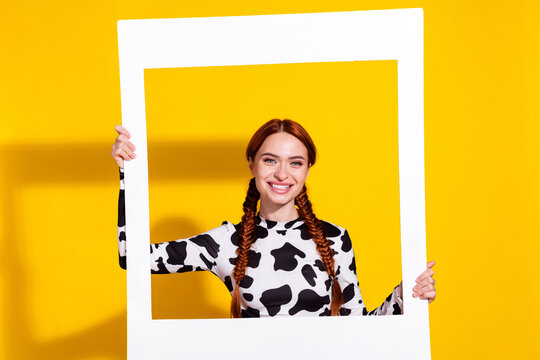 Portrait of positive nice girl toothy smile hands hold paper album card isolated on yellow color background