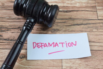 Concept of Defamation write on sticky notes isolated on Wooden Table.