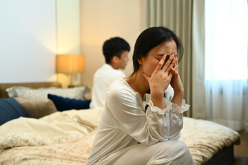 Young woman sitting and crying on bed after argument with her husband. Relationship problems concept