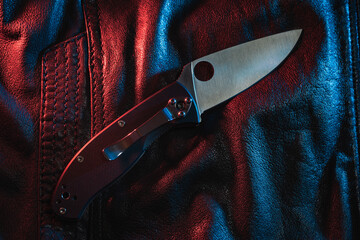 Close-up photo of a pocket folding knife on a leather jacket. - obrazy, fototapety, plakaty