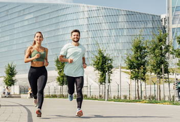 Couple running together in sportswear near modern curved architecture on a clear day.