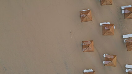 Aerial view sun loungers and straw parasols on seashore. No people morning beach