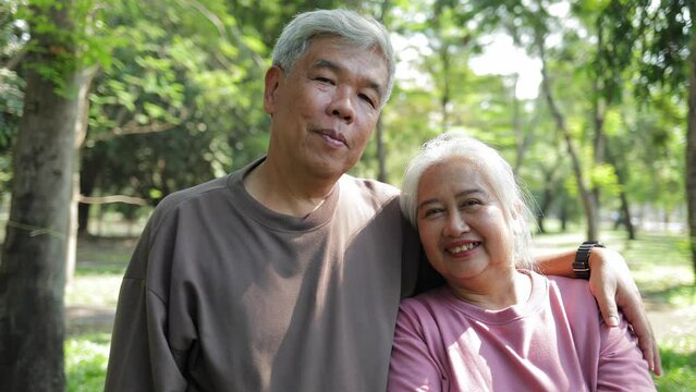 Elderly Asian couple standing and hugging each other in the garden. They smile happily. Living happily in retirement. Health care. Elderly society